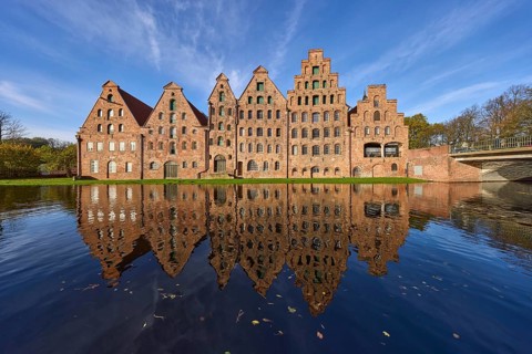 Historic salt warehouses with reflections on the water surface of the Trave, blue sky with veil