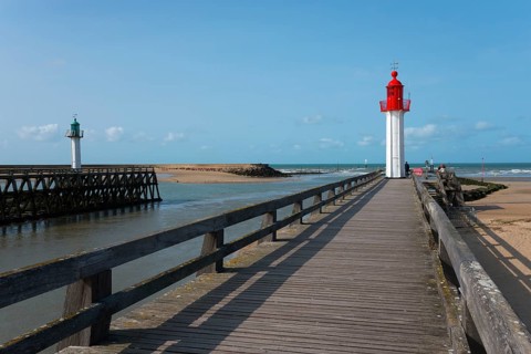 Red and green lighthouses along a wooden walkway on the coast under a blue sky, green lighthouse in