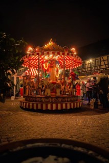 An illuminated carousel at a Christmas market surrounded by half-timbered houses at night,