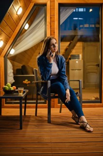 Cute young woman sitting on the terrace of a bungalow late evening and talking on the smartphone