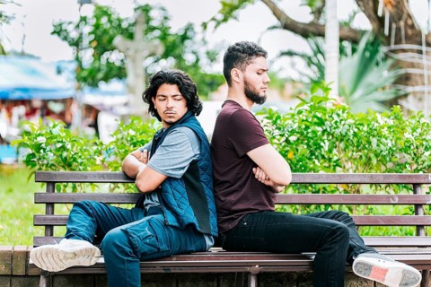 Two angry friends sitting on a park bench. Two friends arguing on a park bench