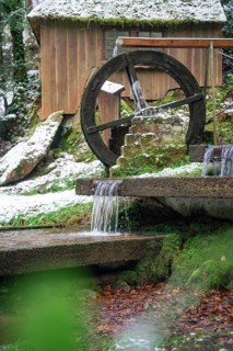 An old water wheel turns next to a hut with snow and running water, spa garden, Bad Wildbad, Black