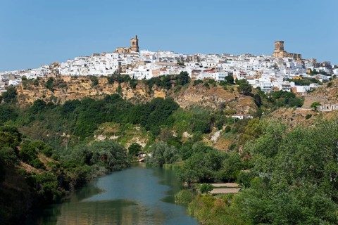 Whitewashed houses on a green hill along a river under a clear sky, Arcos de la Frontera, Guadalete