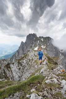 Mountaineer with helmet on a narrow hiking trail on a rocky ridge, ascent to the Maukspitze, clouds