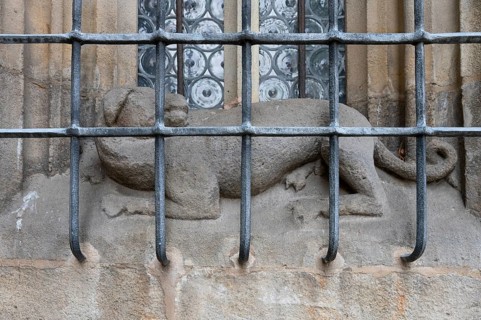 Dog sculpture behind the iron grating of a pointed arch window at the late Gothic hall church of St