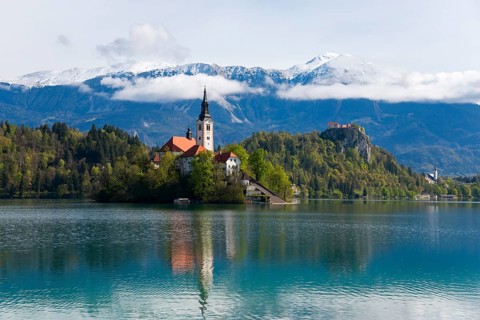 Church on an island in a lake, surrounded by mountains with snow, Bled Island with St Mary's