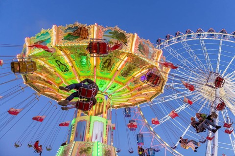 Illuminated chain carousel and Ferris wheel at night with cheerful people, funfair, wave flight,