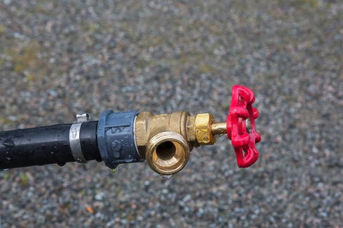 Close-up of black plastic garden hose main water supply connecting pipe with brass fitting and red