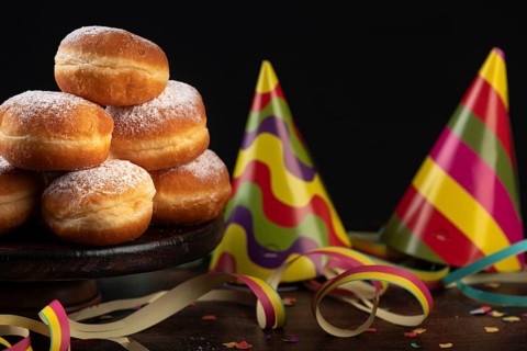 Piles of doughnuts with colourful paper streamers, confetti and party hats on a dark table,