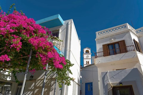 White houses of Menetes with bougainvillea and a bell tower in front of a clear blue sky, Menetes,
