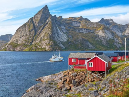 Rorbuer in Hamnoy, fishing boat in front of the mountain Olstinden, blue sky, Moskenesoya, Lofoten,