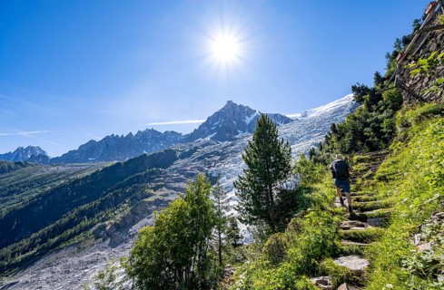 Hiker on hiking trail La Jonction, view of glacier Glacier des Bossons with sun star, behind summit