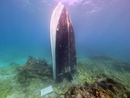 An upright boat underwater, surrounded by sand and coral, in a tranquil atmosphere, dive site John