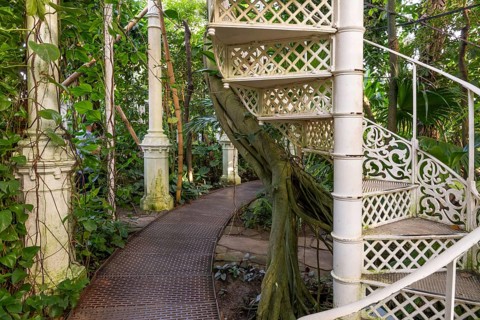 Decorative white spiral staircase and cast iron columns amidst lush vegetation, historic