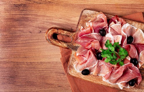 Sliced prosciutto, on a cutting board, with olives and herbs, snack, breakfast, no people