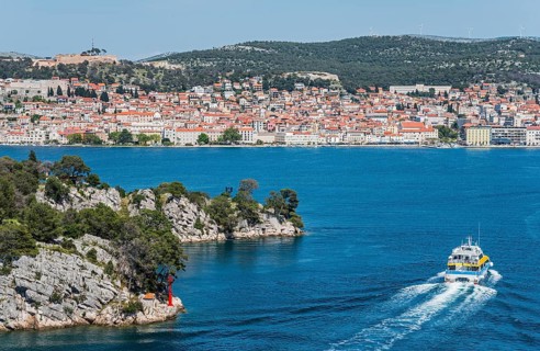 A boat moves through the blue water with a view of a built-up coastal landscape, St Anthony's