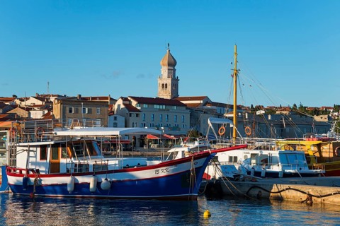 A harbour full of boats and ships with a striking bell tower in the background under a sunny sky,