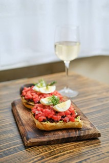 A wooden serving board holds two generous portions of bruschetta topped with diced salmon and egg