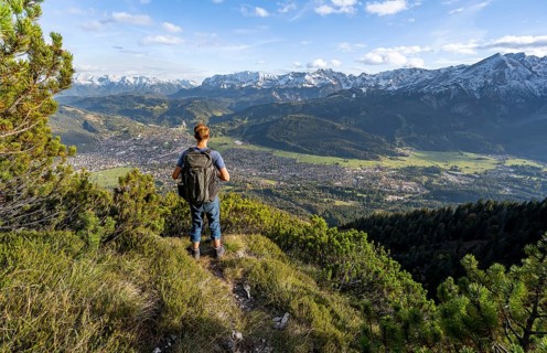 Mountaineer on a narrow hiking trail between mountain pines, view of Garmisch-Partenkirchen and