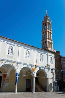 White church building with a high bell tower against a clear blue sky in a city setting, Holy