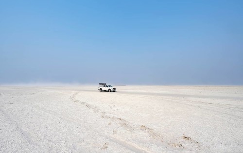 Four-wheel drive Toyota Hilux with roof tent, driving over salt pan, lone car in large wide plain,