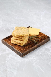 Homemade cheese crackers are neatly stacked on a rustic wooden board. Fresh thyme sprigs accompany