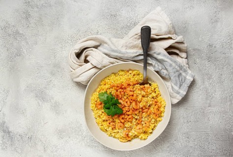 Risotto with shrimp, in a bowl, on a textured surface, with a side dish of fresh coriander,