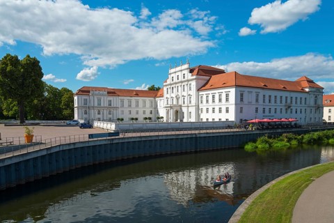 An impressive baroque castle on the riverbank with a canoeist in the water, Oranienburg Castle,