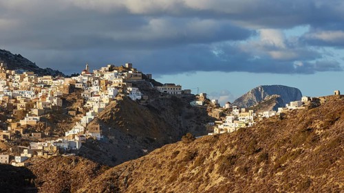 An elongated village under a bright sky with scattered clouds, situated on a hill, Colourful