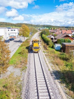 Maintenance vehicle on the railway tracks, surrounded by houses and under a cloud cover, tamping