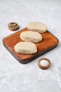 Three breaded cutlets on a rustic wooden cutting board, accompanied by small bowls of salt and