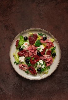 Salad with dried tomatoes, prosciutto, soft cheese, olives, homemade, top view