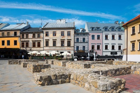 Row of historic houses and stone benches on a sunny square, foundations of St Michael's parish