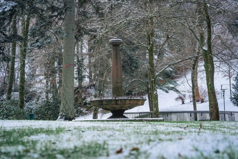 A snow-covered fountain under tall trees in the winter park, spa garden, Bad Wildbad, Black Forest,