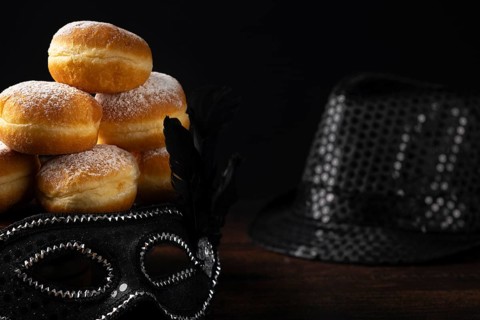 Doughnuts against a dark background next to a black hat and carnival mask