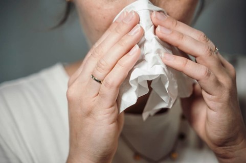 Woman holding a crumpled handkerchief to her nose, possibly with a cold or sneezing, 'symbolic