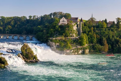 Picturesque landscape with a waterfall, river, bridge and buildings, all in a warm afternoon light,