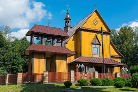 Yellow wooden church with bell tower and red roof, surrounded by trees and sky, Church of the Holy