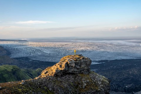 Young man, tourist in front of impressive glacier, in evening light, landscape with mountains and