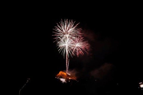 Large fireworks display glows colourfully in the night sky above an illuminated building, New