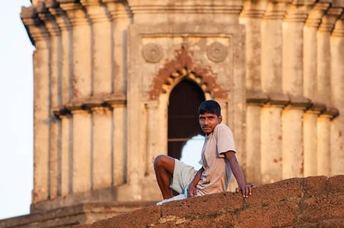 Young man on wall in front of terracotta temple, Bishnupur, Bankura district, West Bengal, India,