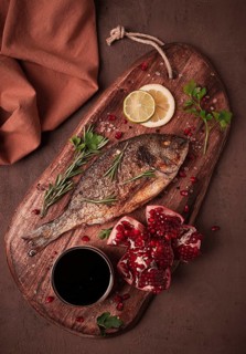 Fried dorado fish, with spices and herbs, on a wooden board, pomegranate sauce, close-up, no people