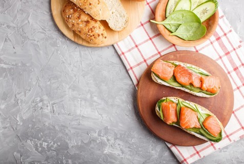 Smoked salmon sandwiches with cucumber and spinach on wooden board on a gray concrete background.
