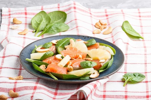 Fresh salmon with pineapple, spinach and cashew on a gray concrete background. Side view, linen