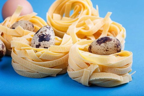Raw uncooked tagliatelle pasta with quail eggs on a blue pastel background. side view, close up
