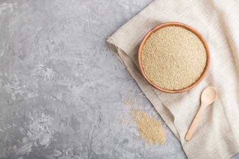 Wooden bowl with raw white quinoa seeds and wooden spoon on a gray concrete background and linen