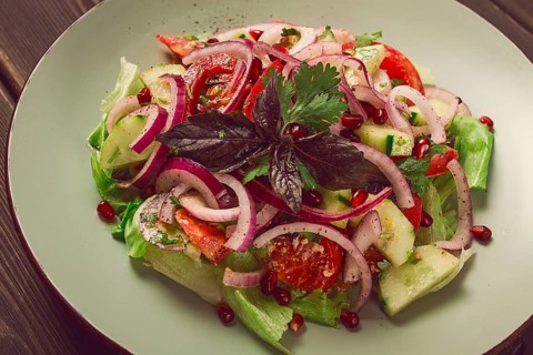 Georgian vegetable salad, tomatoes with cucumbers, red onion, walnut, pomegranate seeds, top view,