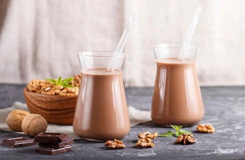 Organic non dairy walnut chocolate milk in glass and wooden plate with walnuts on a black concrete