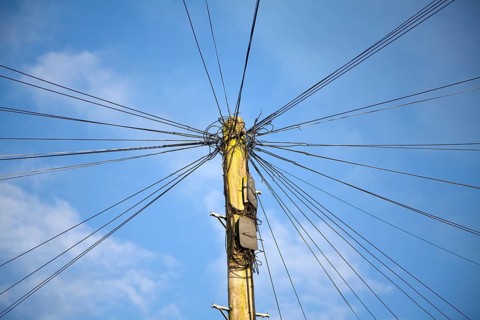 Telephone line cables radiating out fro telegraph pole against blue sky, UK