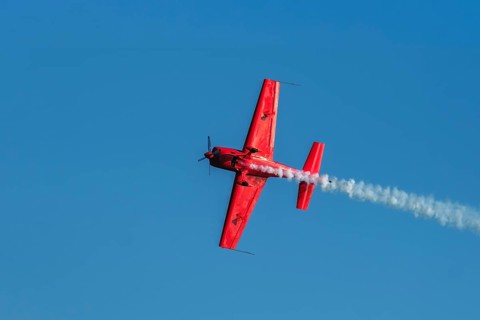 Red stunt aerobatic plane performing stunts in blue sky. Concept of speed, difficulty, precision,